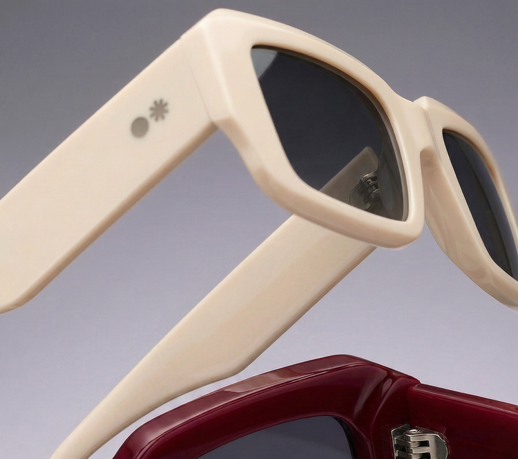 Dos pares de gafas de sol con montura rectangular, una en color crema y otra en granate, sobre fondo gris