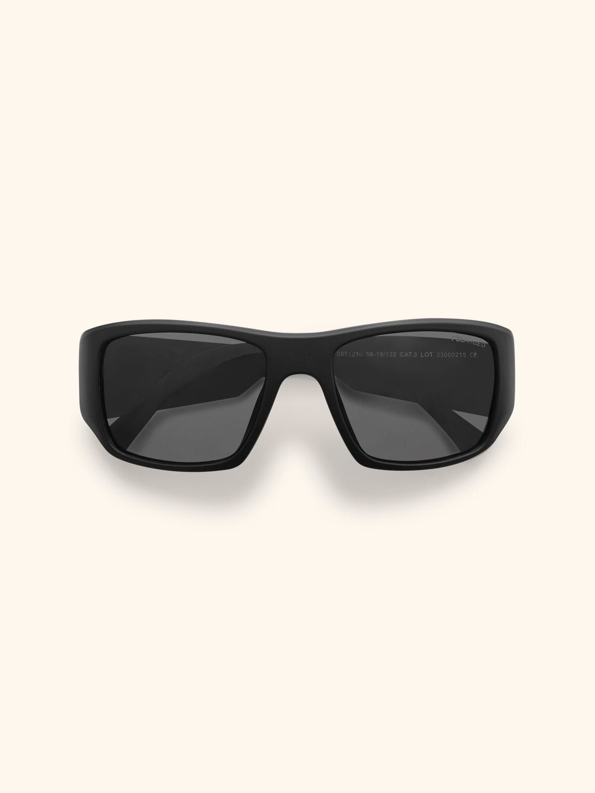 Gafas de sol negras con montura envolvente estilo deportivo y cristales negros, vista frontal sobre fondo crema