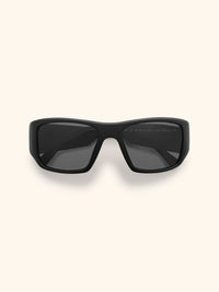 Gafas de sol negras con montura envolvente estilo deportivo y cristales negros, vista frontal sobre fondo crema