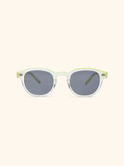 Gafas de sol con montura redondeada transparente y varillas verde lima, cristales grises, vista frontal sobre fondo crema