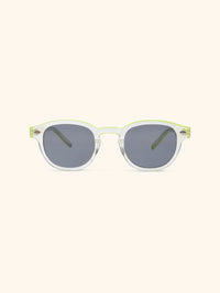Gafas de sol con montura redondeada transparente y varillas verde lima, cristales grises, vista frontal sobre fondo crema